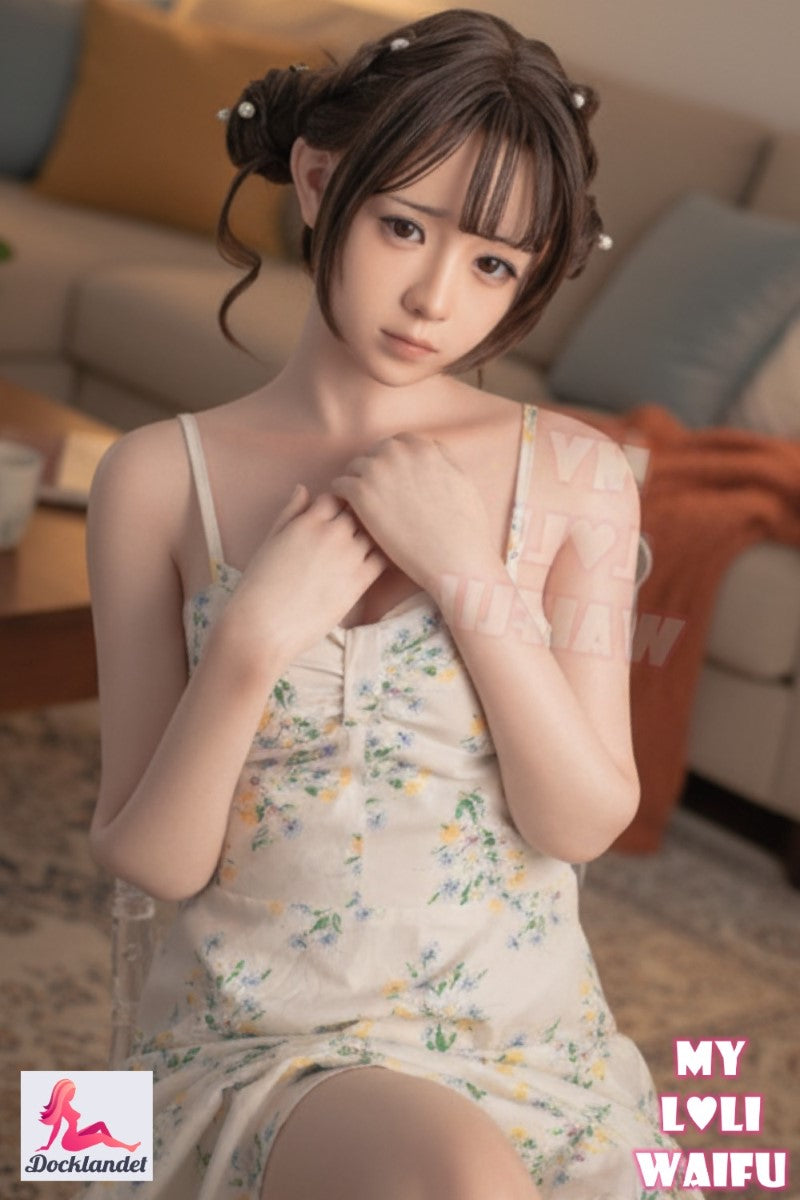 Nanami silikonsexdocka 150 cm, sitter i vit spetsklänning och visar sin kurviga kropp med B-kupa mot ljus studiobakgrund.